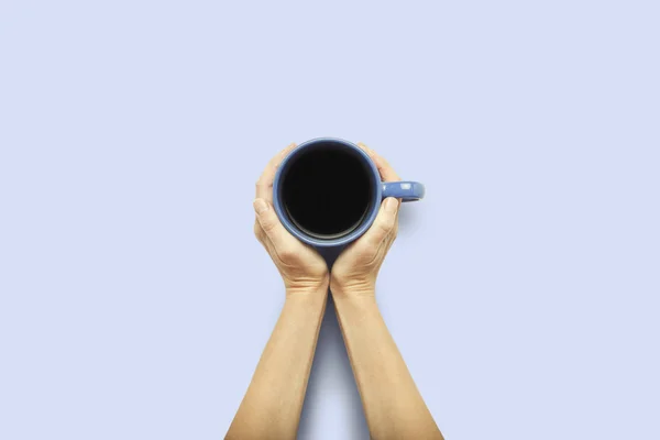 Dos manos sosteniendo una taza con café caliente sobre un fondo azul. Concepto de desayuno con café o té. Buenos días, noche, insomnio. Piso tendido, vista superior — Foto de Stock