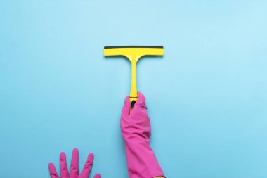 Pembe eldiven windows mavi bir arka plan üzerinde temizlik için bir kazıyıcı tutan el. temizlik hizmet anlayışı. Düz yatıyordu, en iyi görünümü