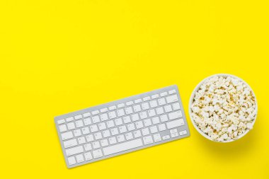 Sarı bir arka planda patlamış mısır ile klavye ve kase. Film izleme kavramı, TV gösterileri, gösterileri, spor online. Düz yatıyordu, üst görünüm.