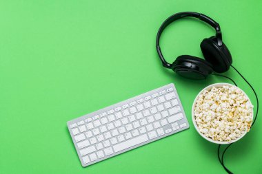 Keyboard, headphones and a bowl of popcorn on a green background. The concept of watching movies, shows, sports on the PS, games online. Flat lay, top view. clipart