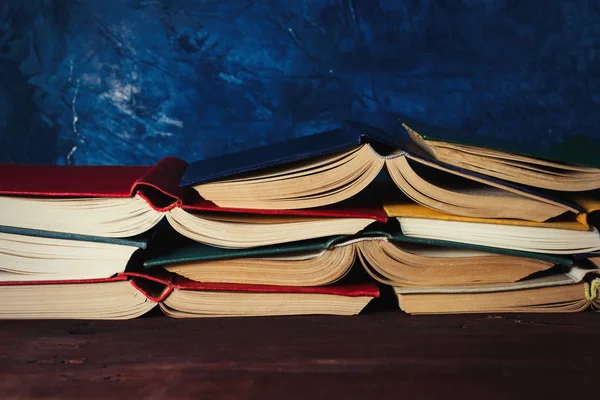 Libros abiertos apilados uno sobre el otro sobre la mesa de madera y el fondo azul oscuro —  Fotos de Stock