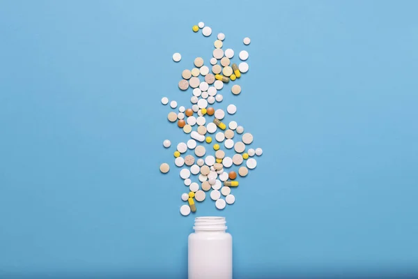 Weiße Flasche und bunte Pillen auf blauem Hintergrund. Konzept der Arzneimittel, Medizin, Medikamente und Behandlung von Krankheiten. flache Lage, Draufsicht — Stockfoto