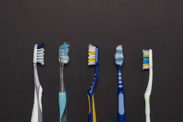 Escovas de dentes usadas de cores diferentes em um fundo preto. Conceito de cuidados orais, higiene pessoal, estomatologia. Deitado plano, vista superior . — Fotografia de Stock