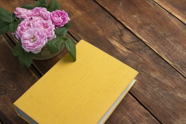 Pink roses and book with yellow cover on a wooden background