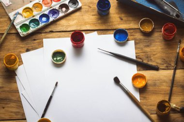 Ressamın işyeri, ahşap bir arka planda suluboya boya, guaj, fırça ve kağıt yapraklarıyla. Uzayı kopyala Düz yatış, üst görünüm