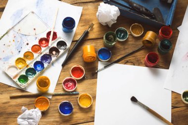 Sanatçının işyeri suluboya boya, guaj, fırçalar ve kağıt sayfalarının ahşap arka plan üzerinde. Yaratıcı atölye kavramı. Uzay kopyalayın. Düz yatıyordu, en iyi görünümü