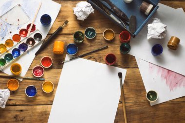 Sanatçının işyeri suluboya boya, guaj, fırçalar ve kağıt sayfalarının ahşap arka plan üzerinde. Yaratıcı atölye kavramı. Uzay kopyalayın. Düz yatıyordu, en iyi görünümü