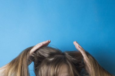 Kız saçlarını ellerinin üzerinde mavi bir arka plan olarak düzeltiyor. Bir saç modeli için hazırlanıyor. Modern tarz