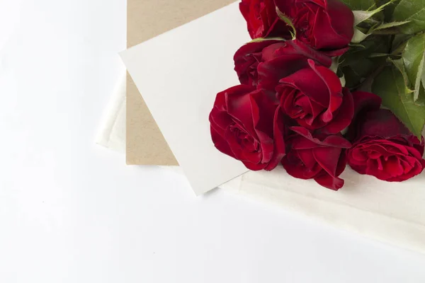 Ramo de rosas rojas y un sobre con una nota sobre un fondo blanco. Concepto de un regalo romántico para un ser querido. Temas de boda — Foto de Stock
