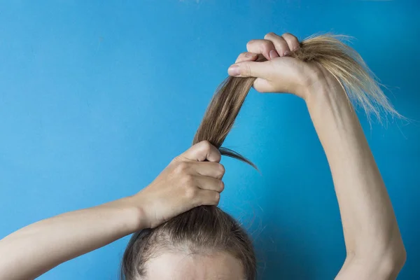 Mädchen bereitet ihr Haar zu einer Frisur mit den Händen auf blauem Hintergrund. moderner Stil — Stockfoto