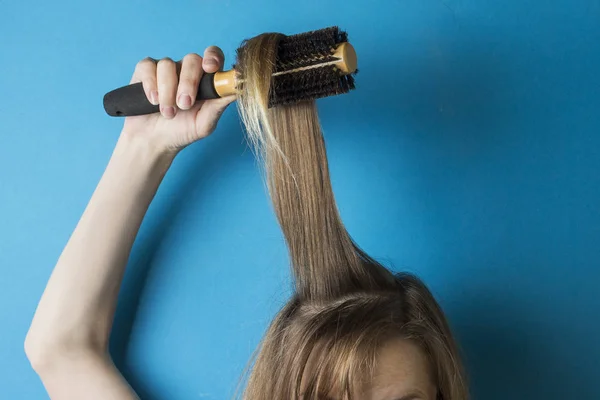 Κορίτσι χτένες τα μαλλιά με μια χτένα για να δημιουργήσετε ένα hairstyle πάνω σε μπλε φόντο. Μοντέρνο στυλ. Ύφος μινιμαλισμού — Φωτογραφία Αρχείου