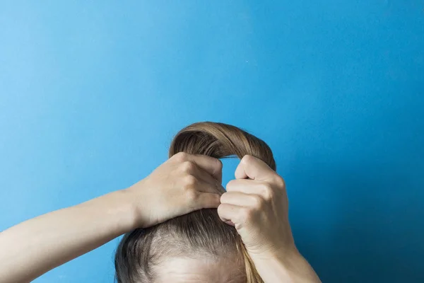 Κορίτσι ισιώνει την ανακατεμένη ουρά των μαλλιών στο κεφάλι της, σε ένα μπλε φόντο. Μοντέρνο γρήγορο χτένισμα. Μαλλιά δεμένα με λάστιχο — Φωτογραφία Αρχείου