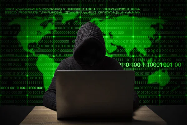 Hacker em uma jaqueta com um capuz com um laptop se senta à mesa. Adicionado ícones de roubo de identidade, sequestro de conta, roubo de dados bancários e mapa do mundo — Fotografia de Stock