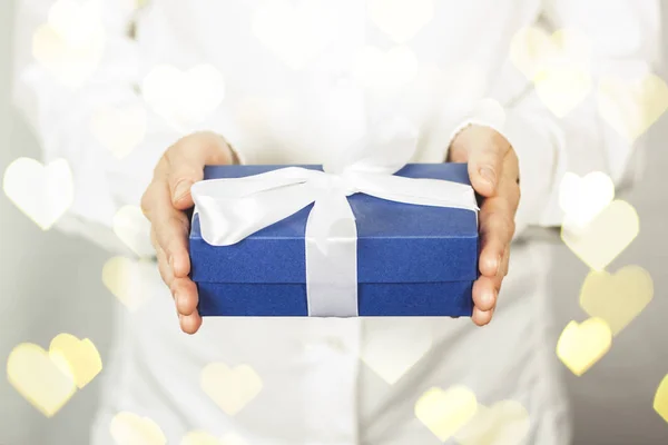 The girl in a white shirt holds a gift. The concept of celebrating a birthday, a new year, christmas, wedding. Getting a gift from a loved one. Added bokeh heart. — Stock Photo, Image