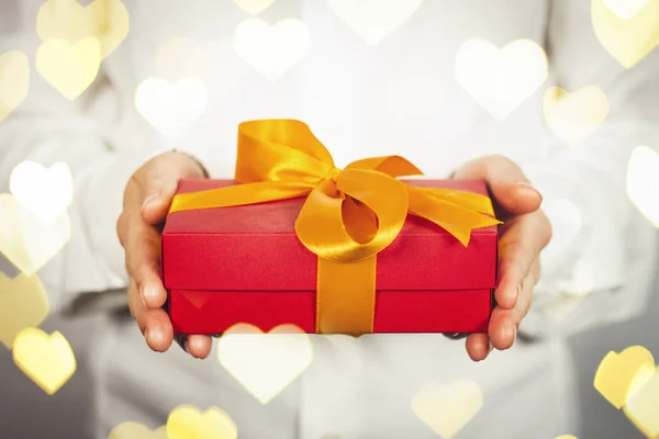 The girl in a white shirt holds a gift. The concept of celebrating a birthday, a new year, christmas, wedding. Getting a gift from a loved one. Added bokeh heart. — Stock Photo, Image