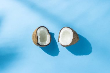 Gölgeler ile doğal ışık altında mavi bir arka plan üzerinde Kırık hindistan cevizi. Sert ışık. Diyet kavramı, sağlıklı beslenme, tropik dinlenme, tatil ve seyahat, vitaminler. Düz döşeme, üst görünüm.