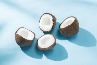 Gölgeler ile doğal ışık altında mavi bir arka plan üzerinde Kırık hindistan cevizi. Sert ışık. Diyet kavramı, sağlıklı beslenme, tropik dinlenme, tatil ve seyahat, vitaminler.