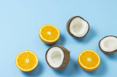 Mavi bir arka plan üzerinde kesilmiş portakal ve hindistan cevizi. Tropikal meyve kavramı, tatil ve seyahat, diyet ve kilo kaybı.