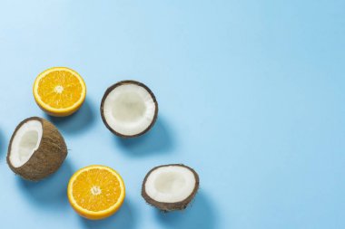 Mavi bir arka plan üzerinde kesilmiş portakal ve hindistan cevizi. Tropikal meyve kavramı, tatil ve seyahat, diyet ve kilo kaybı.