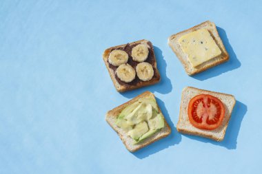 Mavi bir arka plan üzerinde peynir, domates, muz ve avokado ile Sandviçler. Sağlıklı beslenme kavramı, otelde kahvaltı, diyet. Doğal aydınlatma, sert ışık. Düz döşeme, üst görünüm.