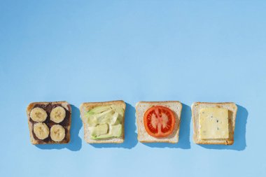 Mavi bir arka plan üzerinde peynir, domates, muz ve avokado ile Sandviçler. Sağlıklı beslenme kavramı, otelde kahvaltı, diyet. Doğal aydınlatma, sert ışık. Düz döşeme, üst görünüm.