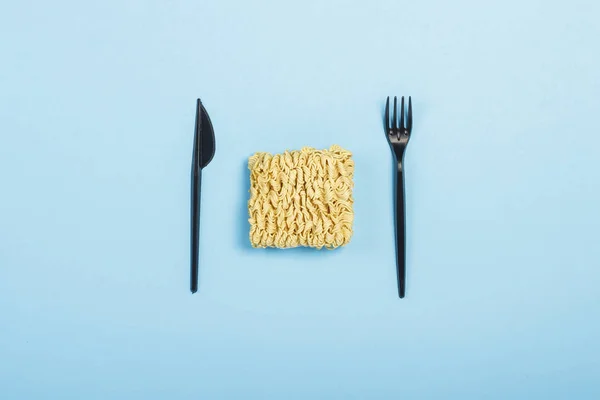 Asian instant noodles and plastic disposable dishes on a blue background. The concept of convenience foods, fast food, junk food. Flat lay, top view.
