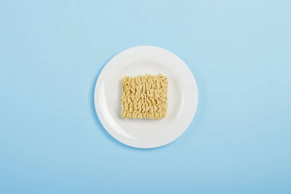 Macarrão instantâneo asiático em uma placa branca contra um fundo azul. O conceito de alimentos de conveniência, fast food, junk food. Deitado plano, vista superior . — Fotografia de Stock