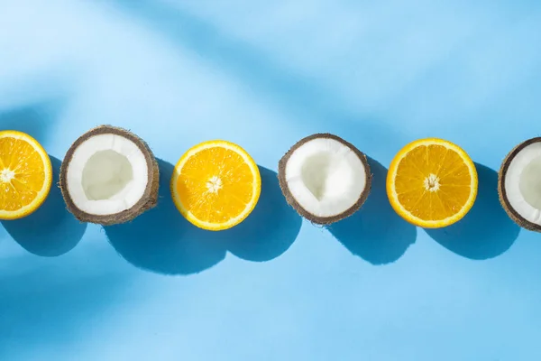 Naranjas y coco sobre un fondo azul bajo luz natural con sombras. Luz dura. Concepto de dieta, alimentación saludable, descanso en los trópicos, vacaciones y viajes. Piso tendido, vista superior . — Foto de Stock