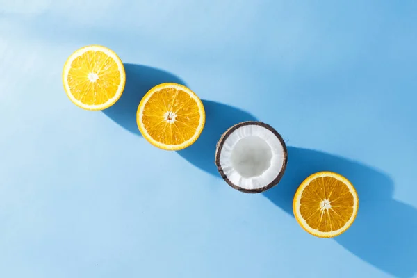 Cortar las naranjas y los cocos sobre un fondo azul. Luz dura. Concepto tropical, comida saludable, desayuno, dieta, vacaciones. Piso tendido, vista superior . — Foto de Stock