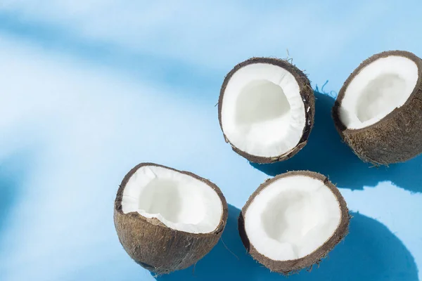 Noix de coco cassée sur fond bleu sous la lumière naturelle avec des ombres. Lumière dure. Concept de régime alimentaire, saine alimentation, repos sous les tropiques, vacances et voyages, vitamines . — Photo