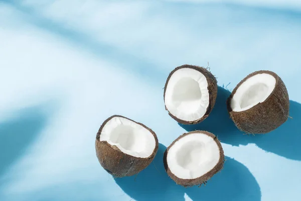 Noix de coco cassée sur fond bleu sous la lumière naturelle avec des ombres. Lumière dure. Concept de régime alimentaire, saine alimentation, repos sous les tropiques, vacances et voyages, vitamines . — Photo