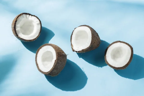 Noix de coco cassée sur fond bleu sous la lumière naturelle avec des ombres. Lumière dure. Concept de régime alimentaire, saine alimentation, repos sous les tropiques, vacances et voyages, vitamines . — Photo