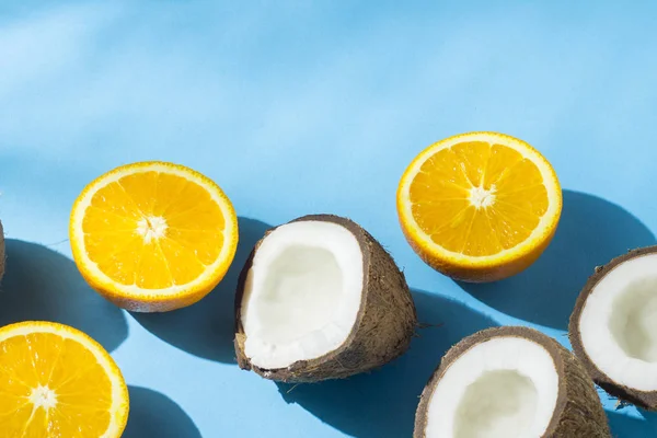 Oranges et noix de coco sur fond bleu sous lumière naturelle avec ombres. Lumière dure. Concept de régime alimentaire, alimentation saine, vacances sous les tropiques, vacances et voyages . — Photo