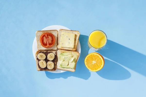 Сэндвичи на белой тарелке, стакан с апельсиновым соком, синий фон. Концепция здорового питания, завтрак в отеле, диета. Естественное освещение, жесткий свет. Плоский, вид сверху . — стоковое фото