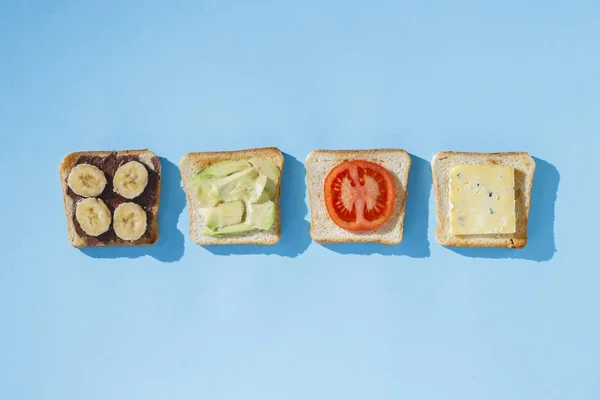 Sandwiches mit Käse, Tomaten, Bananen und Avocado auf blauem Hintergrund. Konzept der gesunden Ernährung, Frühstück im Hotel, Ernährung. natürliches Licht, hartes Licht. flache Lage, Draufsicht. — Stockfoto
