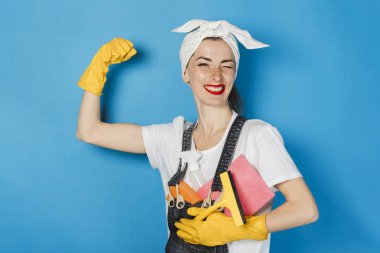 Başında atkı olan genç bir kız, sarı lastik eldivenler kolunda mavi bir arka plan akar. Temizlik ve temizlik hizmeti kavramı, yüksek kalite.