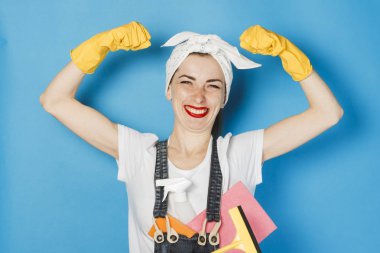 Başında atkı olan genç bir kız, sarı lastik eldivenler kolunda mavi bir arka plan akar. Temizlik ve temizlik hizmeti kavramı, yüksek kalite.