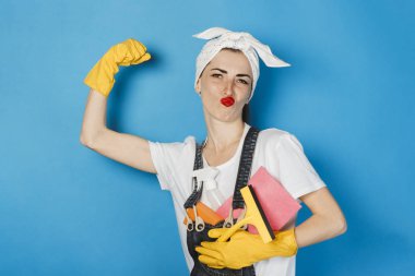 Başında atkı olan genç bir kız, sarı lastik eldivenler kolunda mavi bir arka plan akar. Temizlik ve temizlik hizmeti kavramı, yüksek kalite.