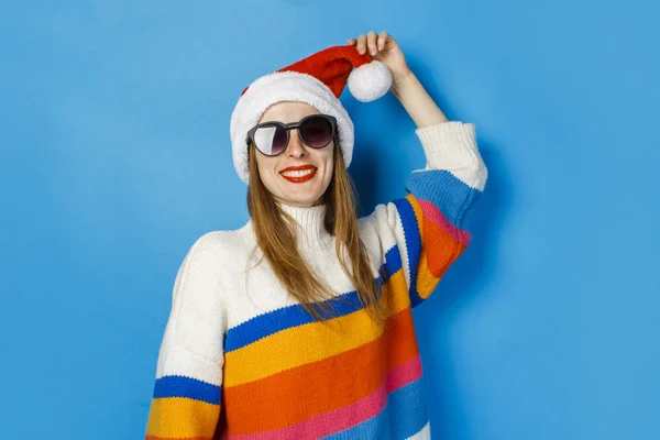 Menina em chapéu de Papai Noel e óculos em um fundo azul. O conceito de Ano Novo e Natal . — Fotografia de Stock