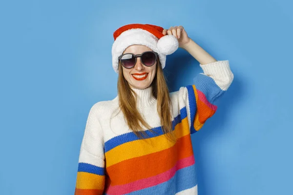 Young girl in Santa Claus hat and glasses on a blue background. The concept of New Year and Christmas. — ストック写真