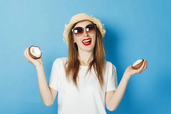 Молодая девушка в очках и соломенной шляпе с кокосом на синем фоне. Концепция отдыха, туристическая поездка, лето и тропики, летнее время . — стоковое фото