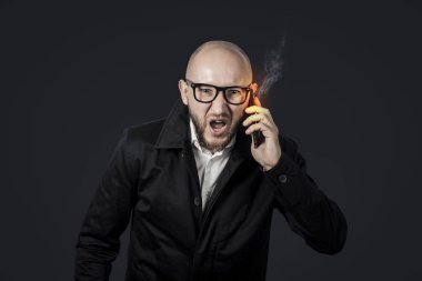 Beyaz gömlek ve koyu pelerin li kötü bir yüz ile erkek işadamı konuşuyor ve karanlık bir arka plan üzerinde telefonla bağırıyor. Kavram stresi, kötü iş, öfke, çok fazla telefon görüşmesi.