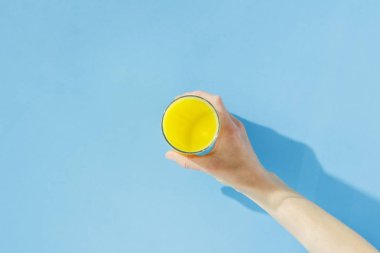 Kadın el mavi bir arka plan üzerinde portakal suyu bir bardak tutan. Vitamin kavramı, tropik, yaz, susuzluk içeceği. Minimalizm. Doğal ışık. Düz döşeme, üst görünüm.