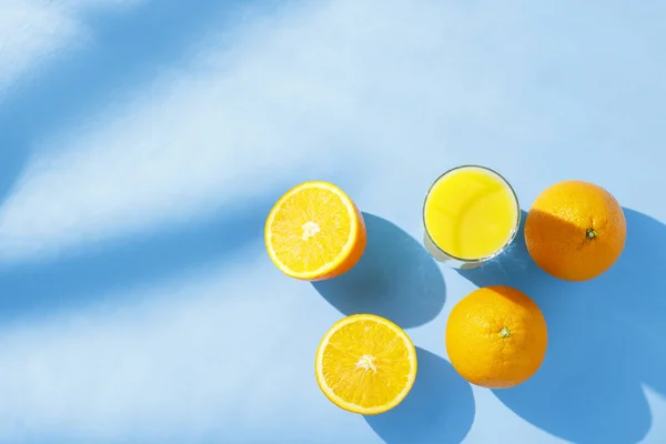 Un vaso de jugo de naranja y naranjas sobre un fondo azul. Concepto de vitaminas, trópico, verano. Luz natural. Piso tendido, vista superior . — Foto de Stock