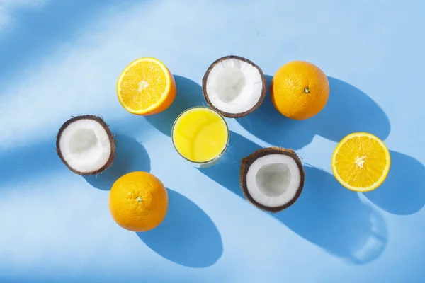 Un vaso de zumo de naranja, naranjas y cocos sobre un fondo azul. Concepto de vitaminas, trópico, verano, bebida de sed. Luz natural. Piso tendido, vista superior . — Foto de Stock