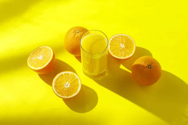 Naranjas y vaso de zumo de naranja sobre fondo amarillo. Concepto de vitaminas, trópico, verano, bebida de sed. Minimalismo. Luz natural. Piso tendido, vista superior . — Foto de Stock