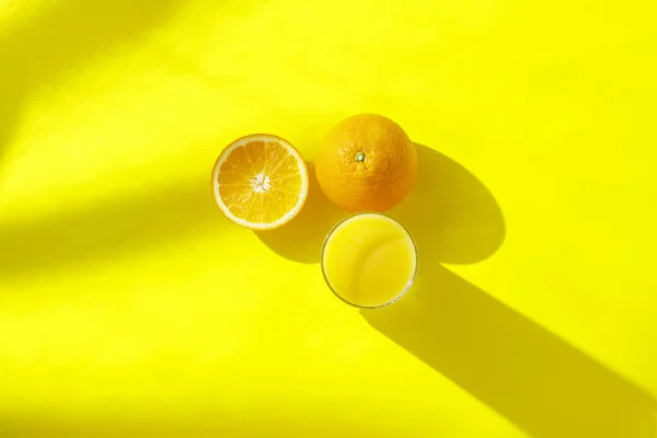 Naranjas y vaso de zumo de naranja sobre fondo amarillo. Concepto de vitaminas, trópico, verano, bebida de sed. Minimalismo. Luz natural. Piso tendido, vista superior . — Foto de Stock