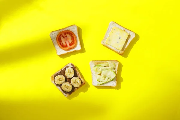 Sandwiches mit Banane, Tomate, Avocado, Blauschimmelkäse auf gelbem Hintergrund. Konzept eines gesunden Frühstücks, Vitamine, richtige Ernährung. natürliches Licht, Schatten von Pflanzen. flache Lage, Draufsicht. — Stockfoto