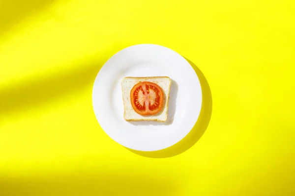 Sanduíche com tomate em uma chapa branca em um fundo amarelo. Conceito de café da manhã saudável, vitaminas, dieta, perda de peso. Flat lay, vista superior — Fotografia de Stock