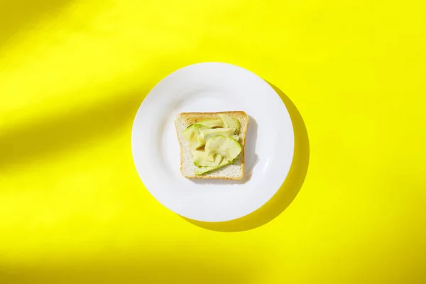 Σάντουιτς με αβοκάντο σε λευκό πιάτο σε κίτρινο φόντο. Υγιεινή αίσθηση πρωινού, βιταμίνες, δίαιτα, απώλεια βάρους. Επίπεδη όψη, κορυφή θέα. — Φωτογραφία Αρχείου